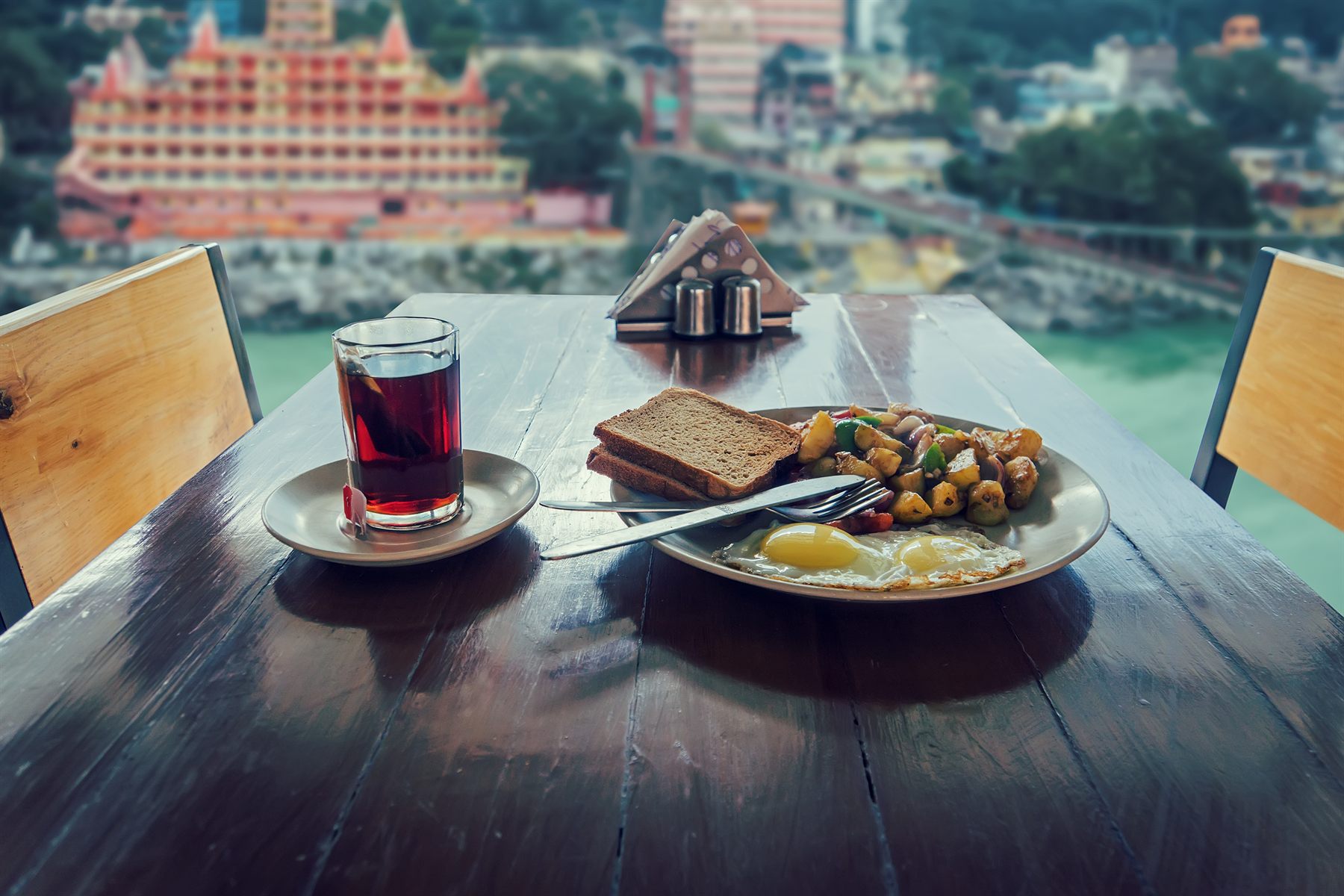 Breakfast of tea, toast and eggs on a table overlooking the river and a tall temple