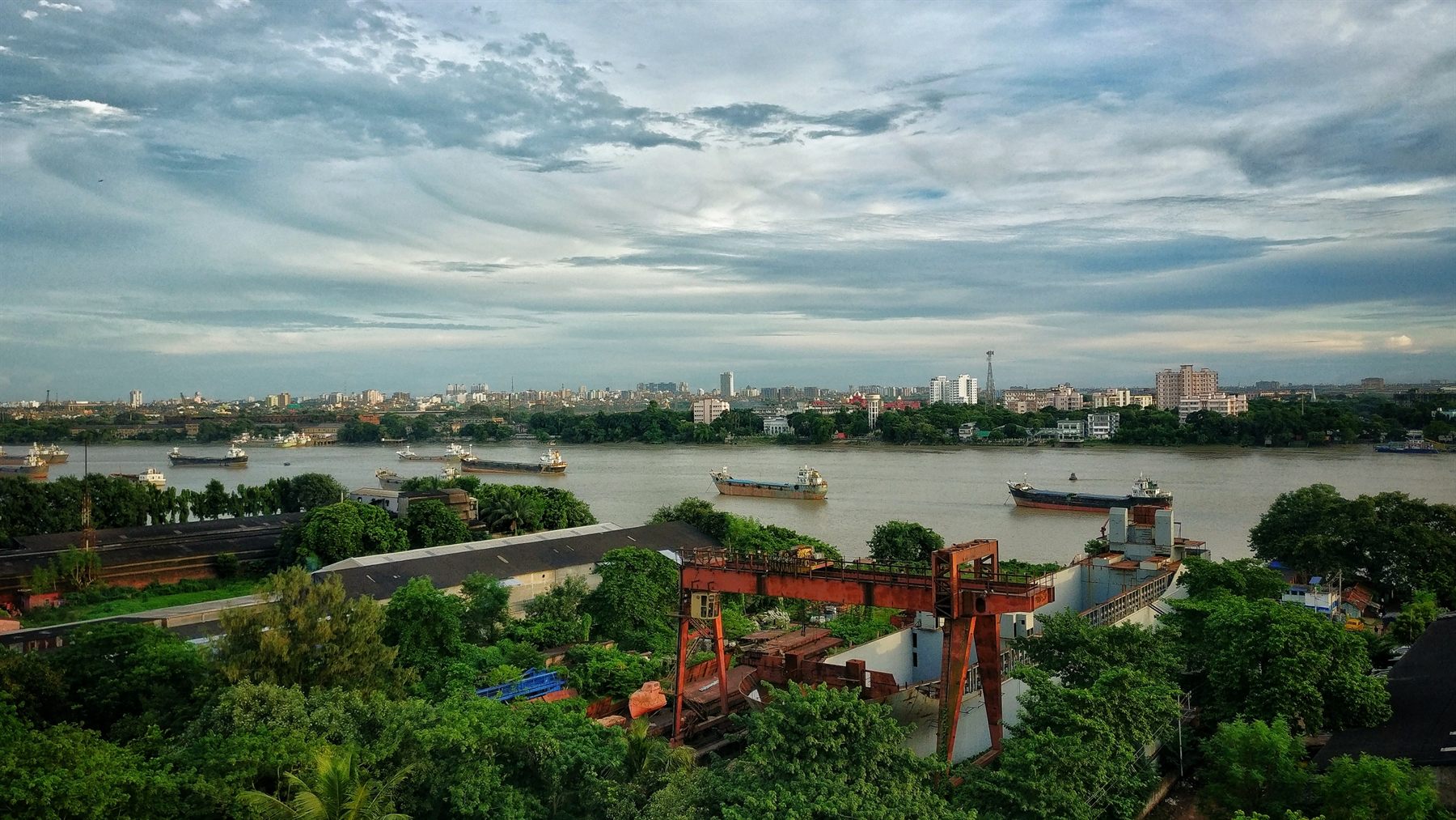 Cargo vessels anchored on a wide river with a city skyline beyond