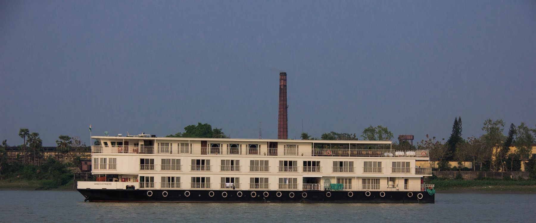 The river cruise ship Ganges Voyager II on the river, a tall brick chimney behind